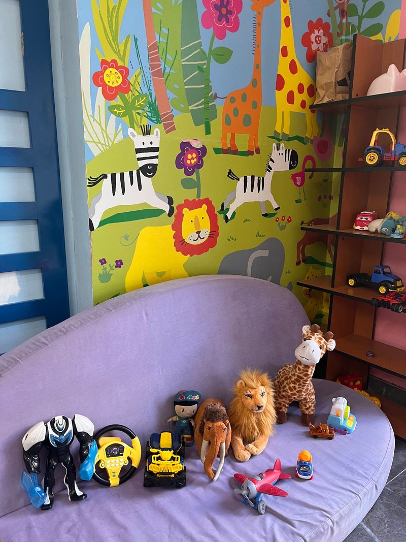 Zürafa ve zebra resimli duvarın önünde mor kanepede oyuncaklar ve peluş hayvanlar